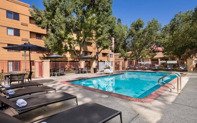 The outdoor pool at Sonesta Select San Jose Airport features a lift, and has nearby sun loungers and shaded tables and chairs.