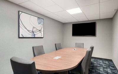 Hotel meeting room, with half a dozen chairs set around a wooden table, and a large TV on the wall.