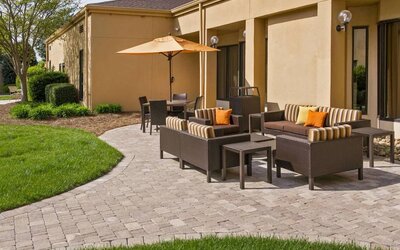 The patio at Sonesta Select Charlotte University Research Park includes sofa and armchair seating, plus coffee tables, near to pleasant greenery.