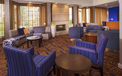 Sonesta Select Charlotte University Research Park’s lobby is furnished with a fireplace, large windows, coffee tables, and comfortable seating.