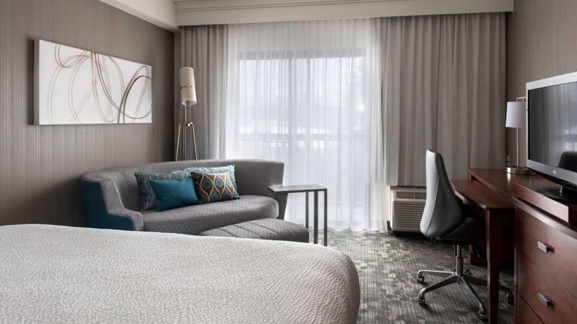 Sonesta Select Boston Milford double bed guest room, featuring sofa, TV, and window.