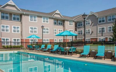 The outdoor pool at Sonesta ES Suites Charlottesville University has a mix of sun loungers and shaded tables and chairs by the side.
