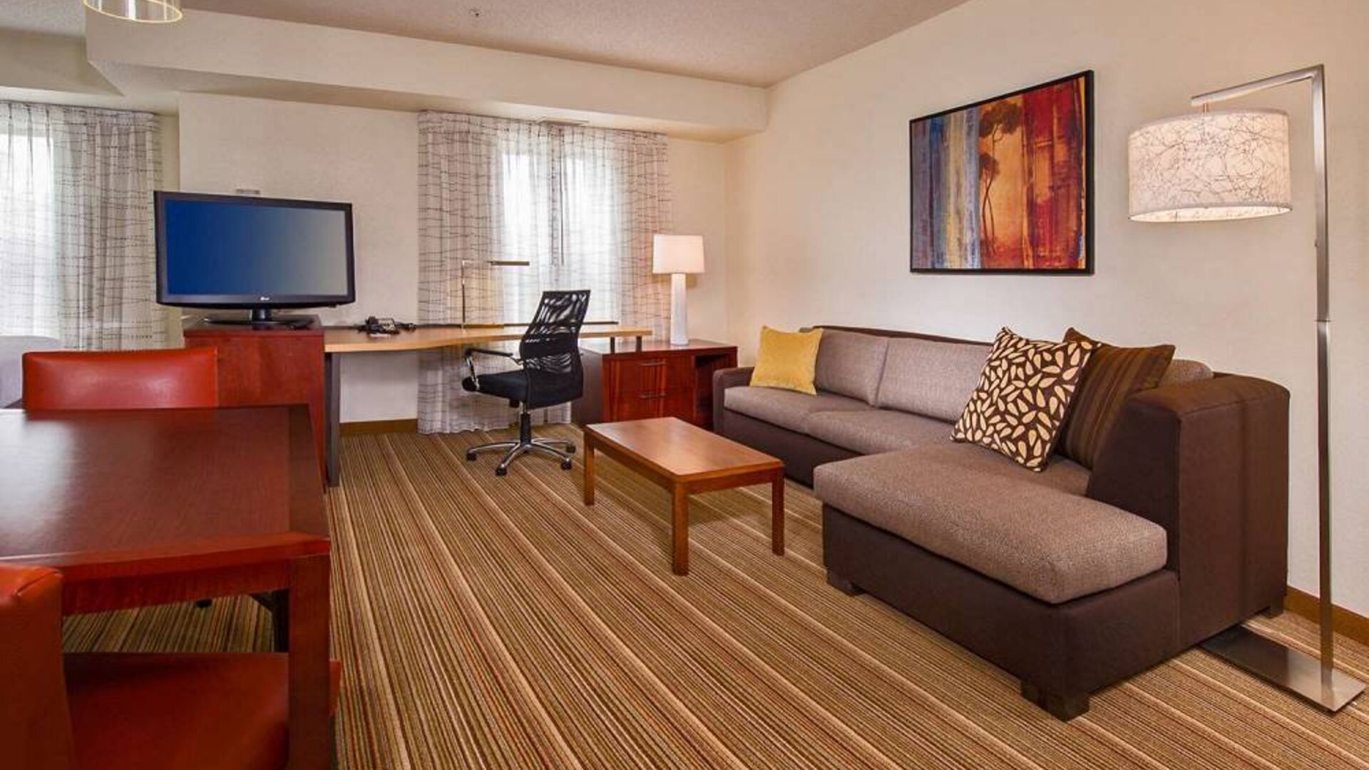 Sonesta ES Suites Charlottesville University guest room workspace, furnished with desk, chair, and TV, plus a sofa.