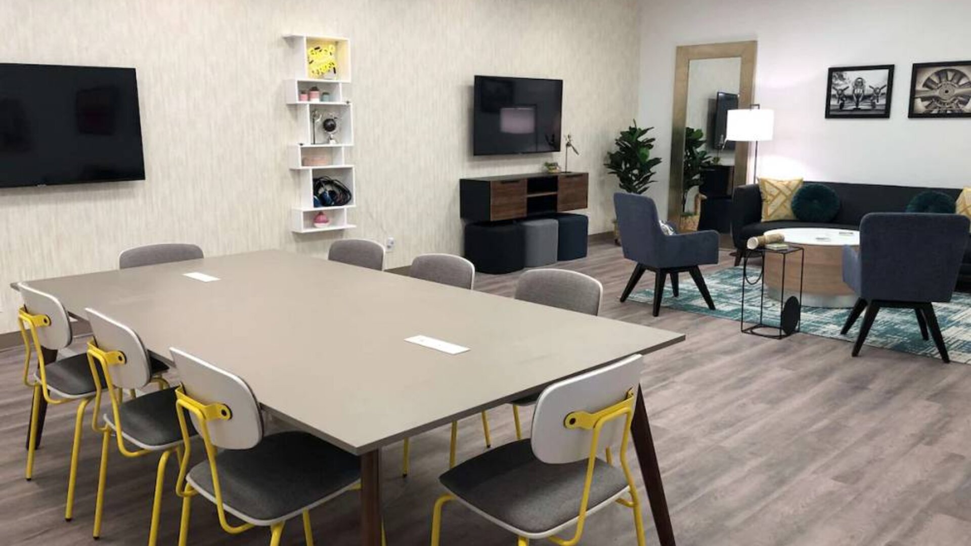 Sonesta Miami Airport meeting room facility, with long table, wall-mounted TV, and nearby armchair and sofa seating. 