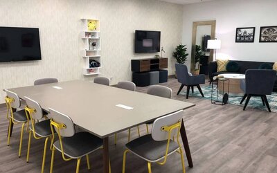 Sonesta Miami Airport meeting room facility, with long table, wall-mounted TV, and nearby armchair and sofa seating. 