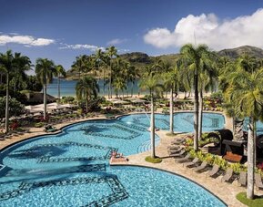 The hotel’s outdoor pool includes sun loungers and tall trees nearby.