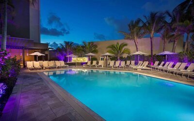 Sonesta Fort Lauderdale Beach’s outdoor pool has palm trees and sun loungers by the side, with shade available.