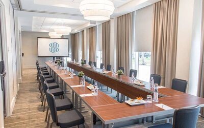 Sonesta Fort Lauderdale Beach meeting room, with a head table for one person and two long tables each with space for 10 attendees, and a projector screen.