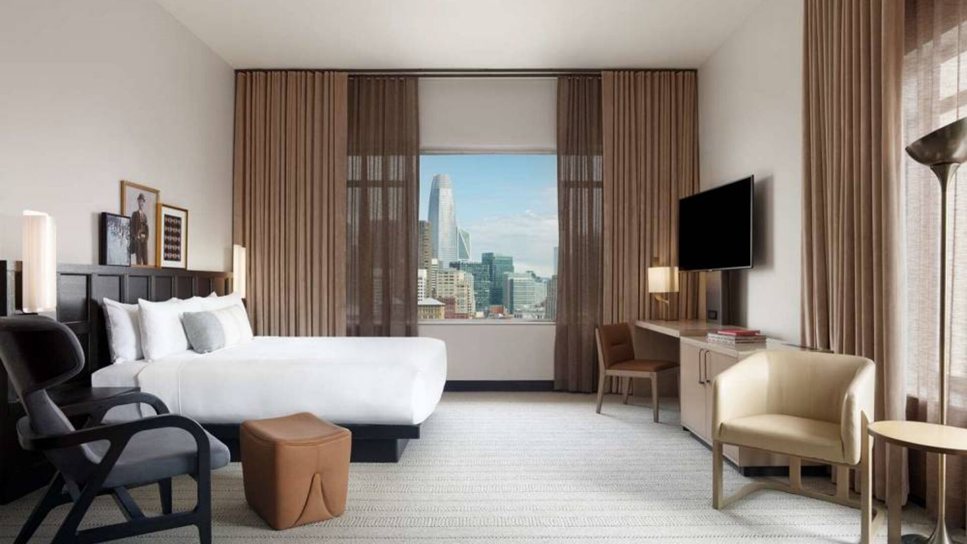 Double bed guest room in The Clift Royal Sonesta, featuring numerous chairs, a desk, coffee table, TV, and window with city views.