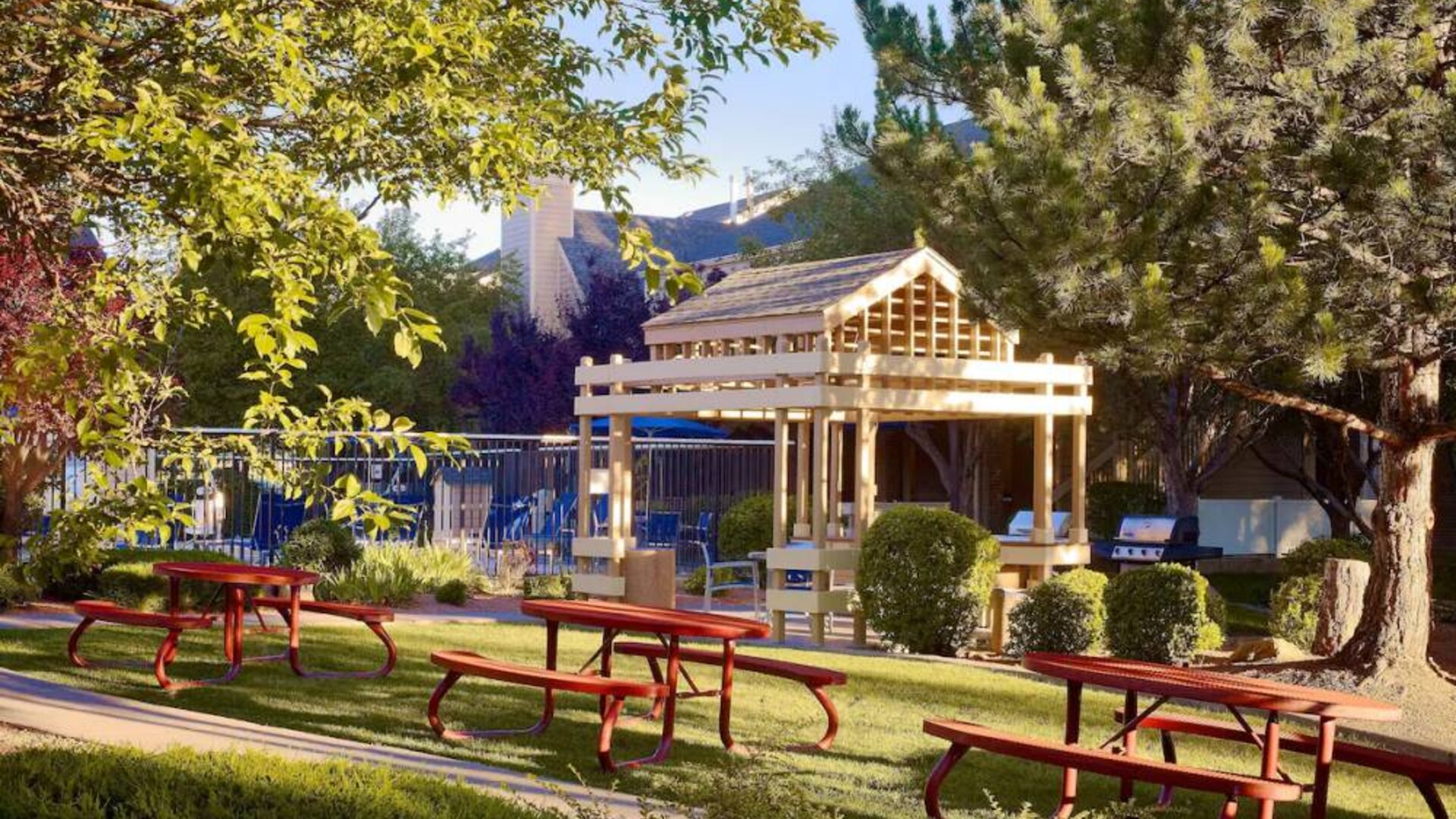The picnic area at Sonesta ES Suites Flagstaff features benches on tables on grass, with trees and and barbecue facilities nearby.