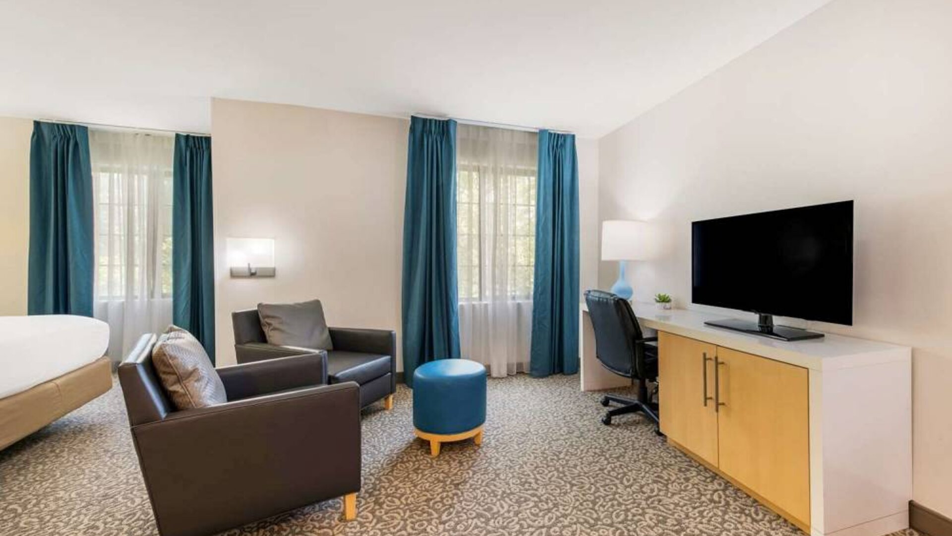 Sonesta ES Suites Charlotte Arrowood guest room workspace desk and chair, with nearby armchairs and television.