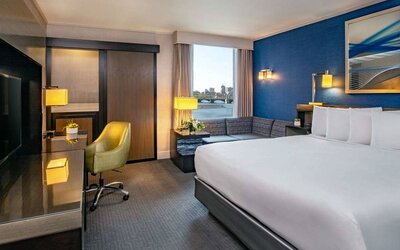 Double bed guest room in Royal Sonesta Boston, furnished with corner sofa and coffee table, comfy chair, and wall-mounted TV.