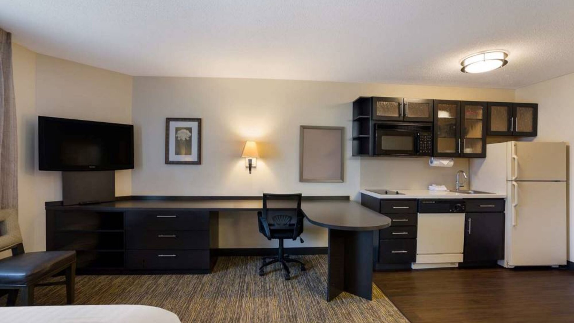 Sonesta Simply Suites Des Moines guest room, furnished with bed, kitchenette, TV, and workspace desk and chair.