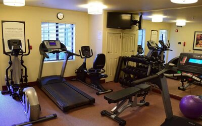 The fitness center of Sonesta ES Suites Portland Vancouver 41st Street has rows of free weights, a wall-mounted TV, and a variety of xercise machines.