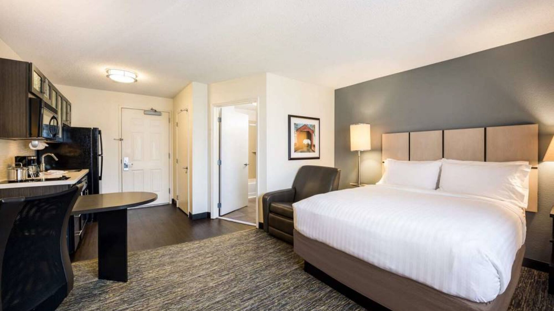 Sonesta Simply Suites Salt Lake City Airport double bed guest room, with kitchen area and an armchair.