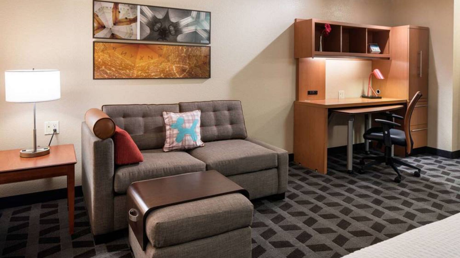 Guest room workspace in Sonesta Simply Suites Seattle Renton, featuring desk, lamp, and chair, with nearby sofa.