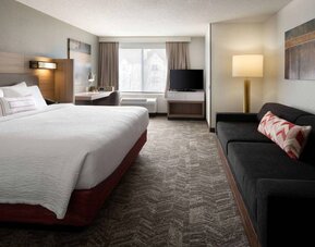 Sonesta Select Seattle Renton double bed guest room, with sofa, workspace desk and chair, TV, and large window.