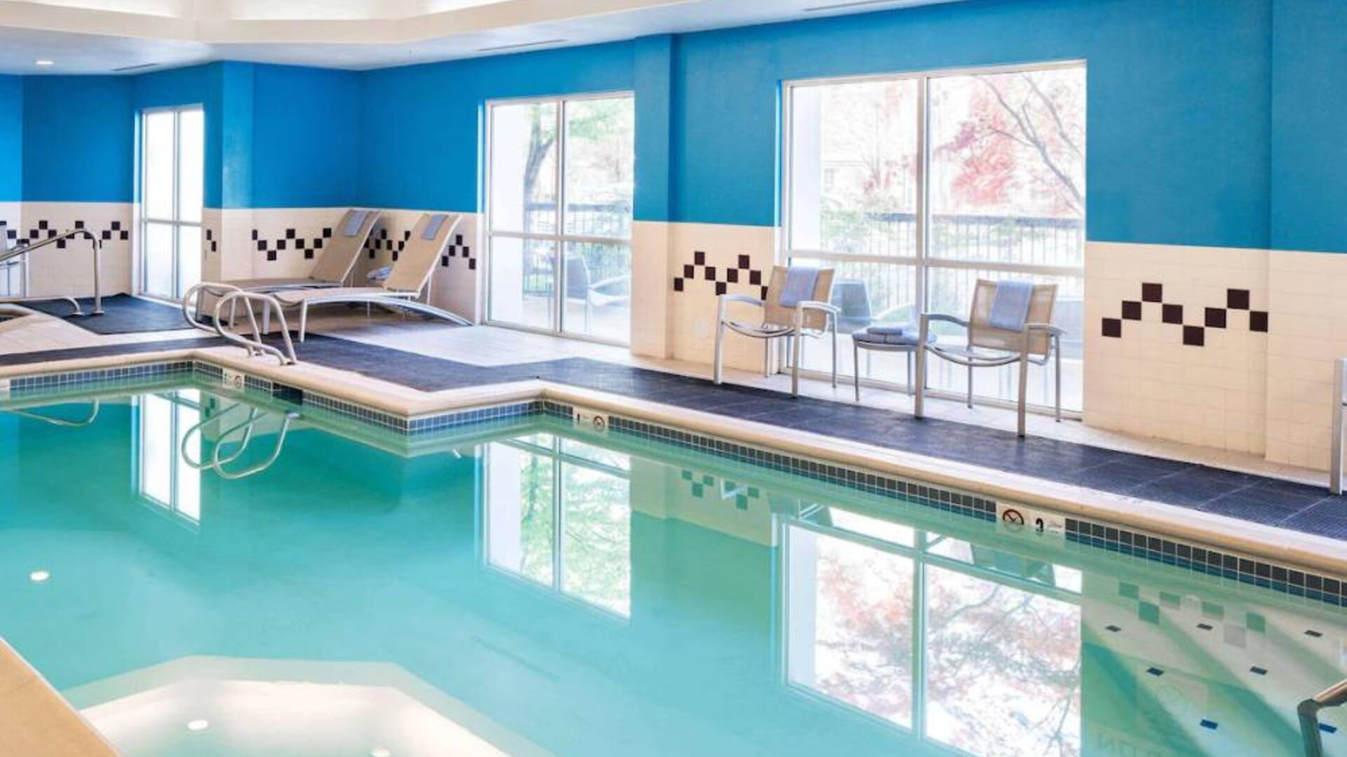 The indoor pool at Sonesta Select Seattle Renton features large windows, and has both chairs and loungers by the side.