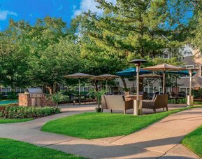 Sonesta ES Suites Parsippany Morris Plains’ barbecue area is furnished with tables and chairs, plus armchair seating, amid numerous trees.