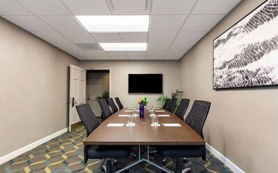 Hotel meeting room, featuring long wooden table, eight swivel chairs, and a large, widescreen TV on the wall.