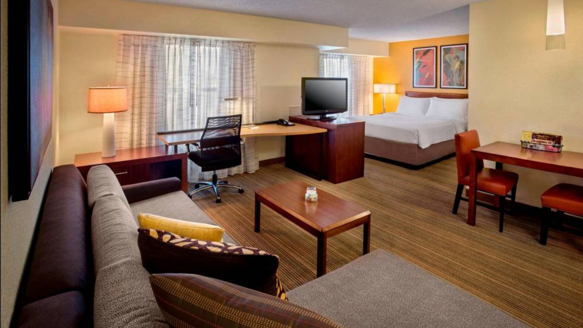 Double bed guest room in Sonesta ES Suites Birmingham Homewood, furnished with TV and sofa, plus workspace desk and chair.