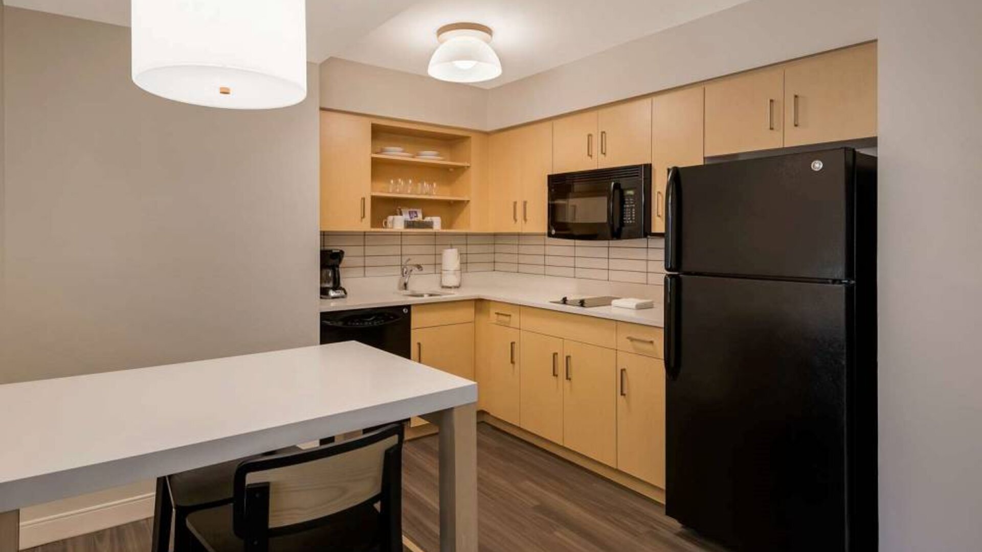 Sonesta ES Suites Andover Boston guest room kitchen, featuring oven, hob, microwave, fridge-freezer, and a kitchen table with two stools.