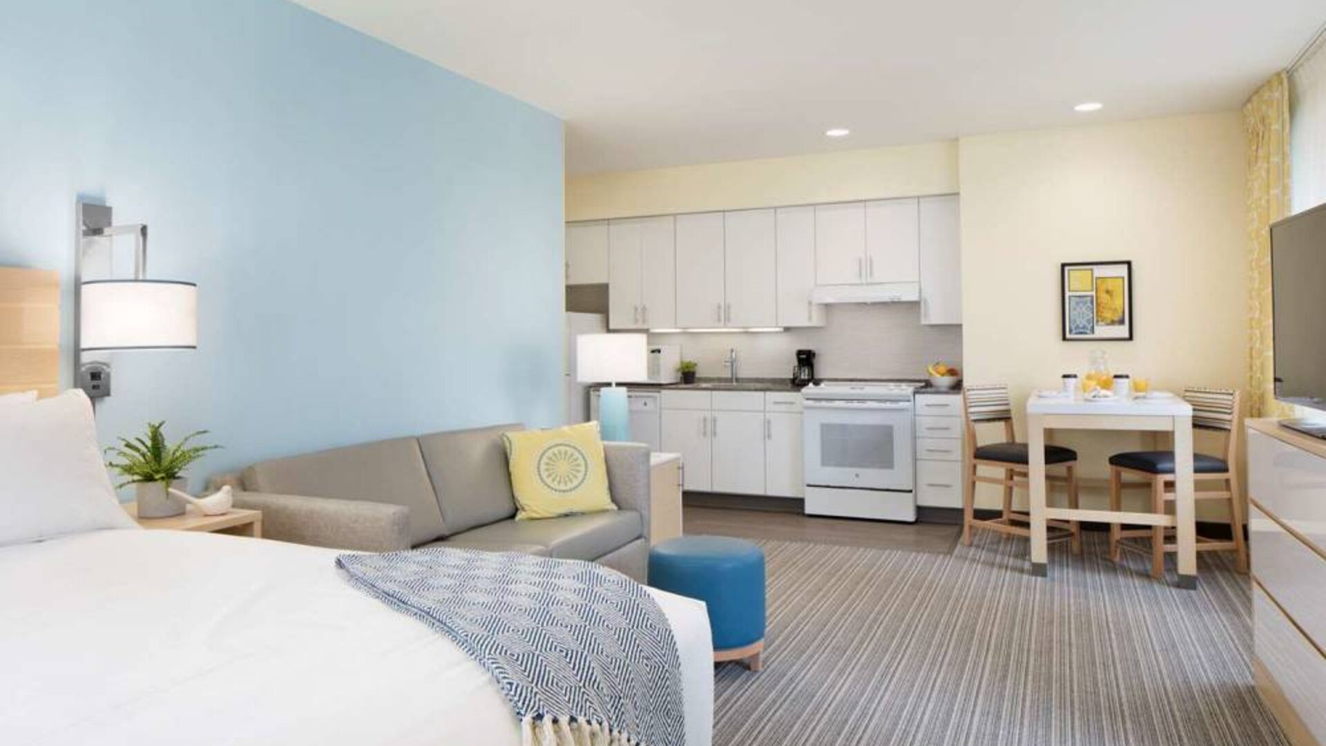 Double bed guest room in Sonesta ES Suites New Orleans, furnished with sofa and TV, plus kitchen area and dining table.