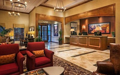 Sonesta Suites Scottsdale Gainey Ranch’s lobby has many potted plants, including cacti, a marble floor, and comfortable armchairs around a coffee table.