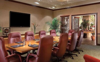 Meeting room in Sonesta Suites Scottsdale Gainey Ranch, furnished with long wooden table, 10 leather chairs, and a wall-mounted widescreen television.