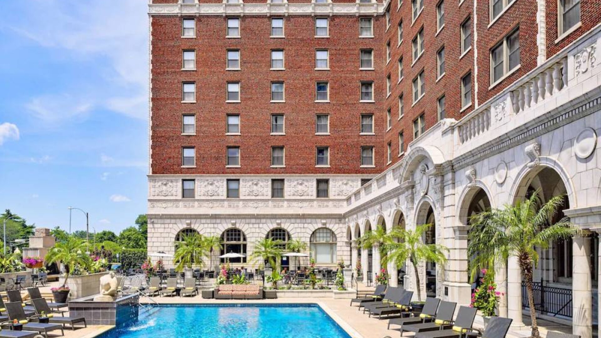 The Chase Park Plaza Royal Sonesta St. Louis’ outdoor pool has rows of sun loungers and potted palm trees by the side, plus sofa seating and a nearby patio.