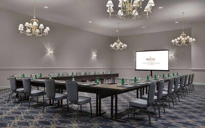 Meeting room in The Chase Park Plaza Royal Sonesta St. Louis, featuring long tables arranged in a U-shape, quartet of chandeliers, seating for over a dozen, and a projector screen.