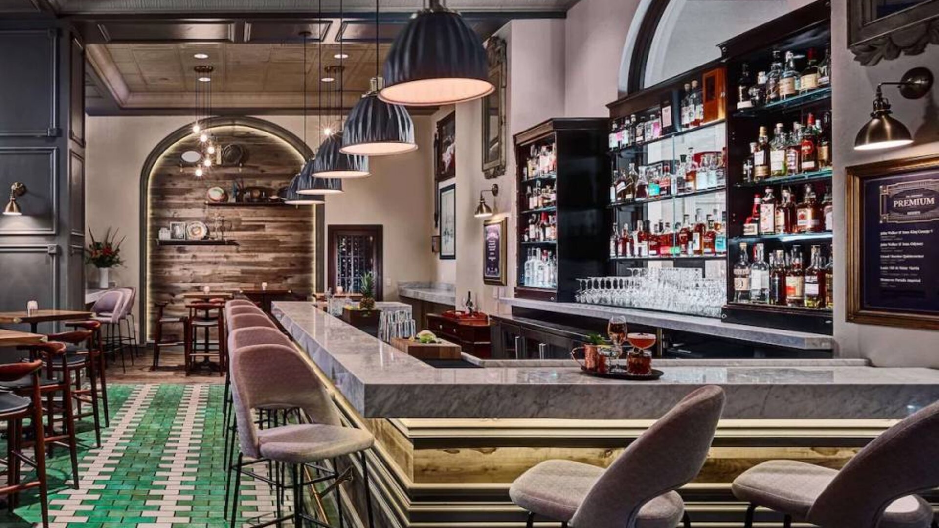 The hotel bar has tall stools available at both the bar itself and at numerous small tables, a hard floor, and a wide array of beverages.