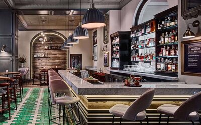 The hotel bar has tall stools available at both the bar itself and at numerous small tables, a hard floor, and a wide array of beverages.