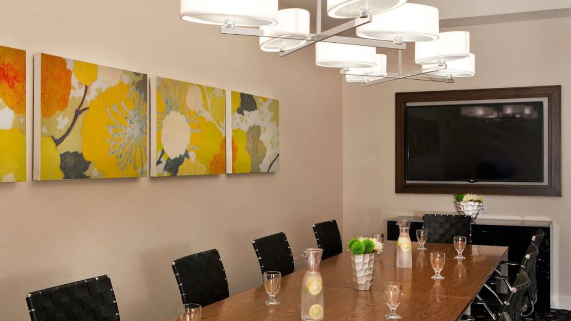 Sonesta Atlanta Airport South meeting room, furnished with long wooden table surrounded by swivel chairs, and art and a widescreen TV on the walls.