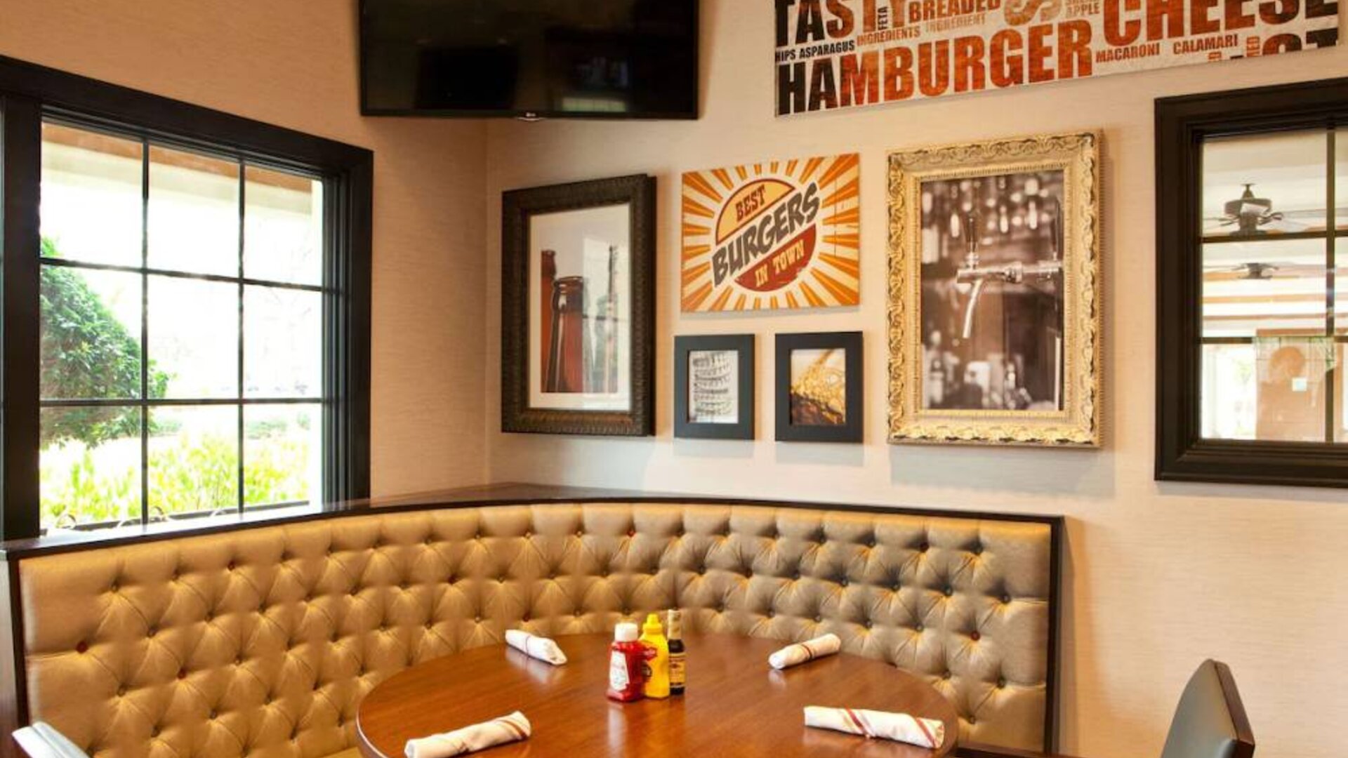 The Burger Place is Sonesta Atlanta Airport South’s on-site restaurant, and includes burger-related art on the wall alongside a widescreen TV, and large windows.
