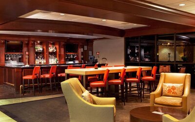 The hotel’s lobby lounge includes armchairs surrounding a coffee table, plus a bar with tall red stools and assorted refreshments.