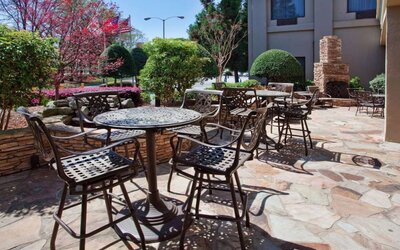 Sonesta Atlanta Airport North’s patio has tables and chairs beside flowers, bushes, and trees.
