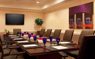 Meeting room in Sonesta Atlanta Airport North, furnished with long wooden table, a dozen chairs, and art and a widescreen television on the walls.