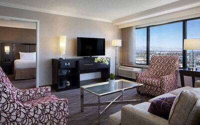 Sonesta San Jose double bed guest room living area, furnished with armchairs, sofa, coffee table, window, and widescreen TV.