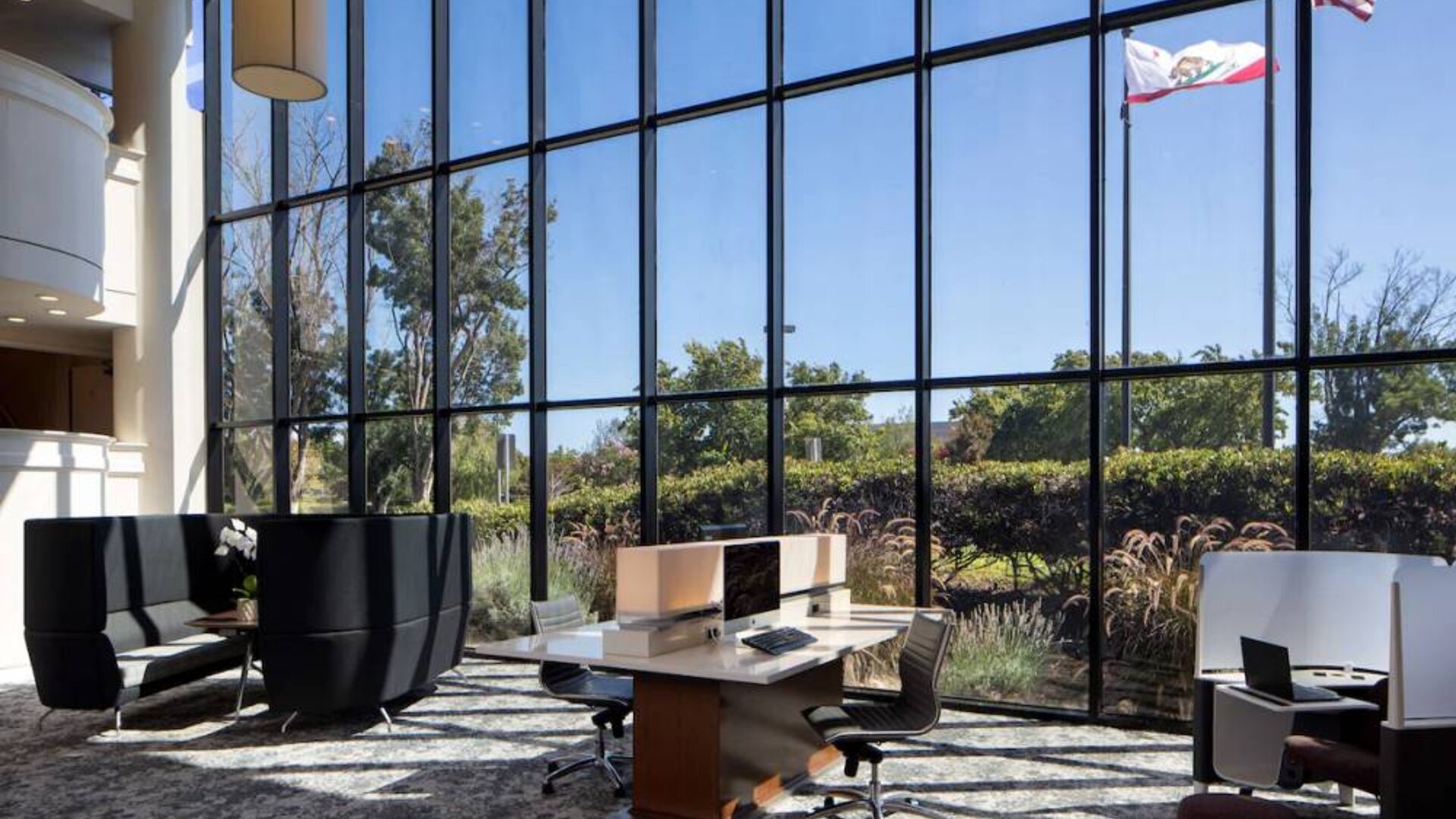 The hotel’s business center has a wall of windows next to it with a view of greenery and flags, while the center itself features multiple workstations and nooks for guests to use.