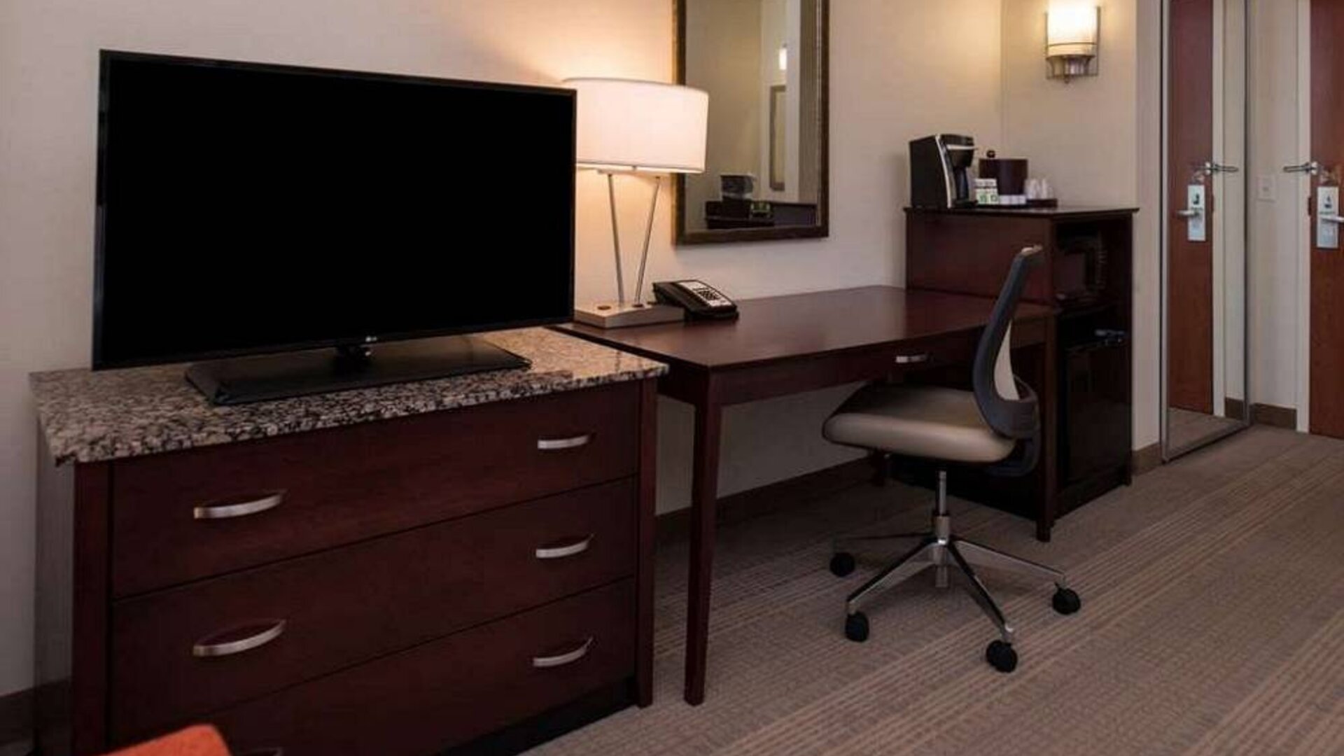 Sonesta Chicago O'Hare Airport Rosemont guest room workspace, including desk, chair, lamp, telephone, and nearby TV.