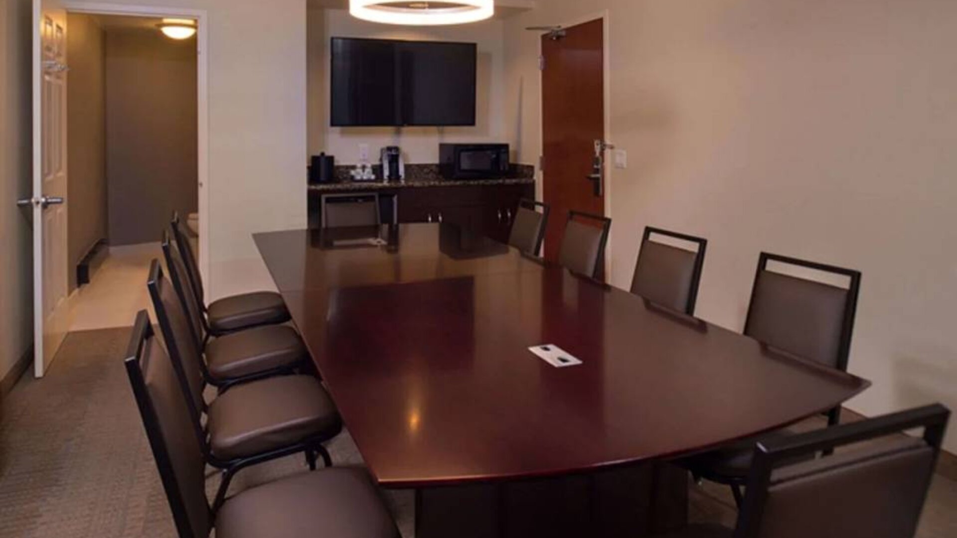 Meeting room in Sonesta Chicago O'Hare Airport Rosemont, featuring long wooden table, 10 chairs, a microwave, and a large TV.