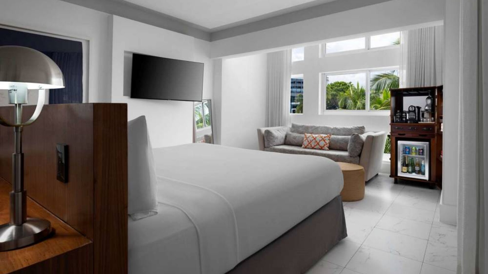 Double bed guest room in Nautilus by Sonesta, with wall-mounted TV, mini-fridge, and a sofa.