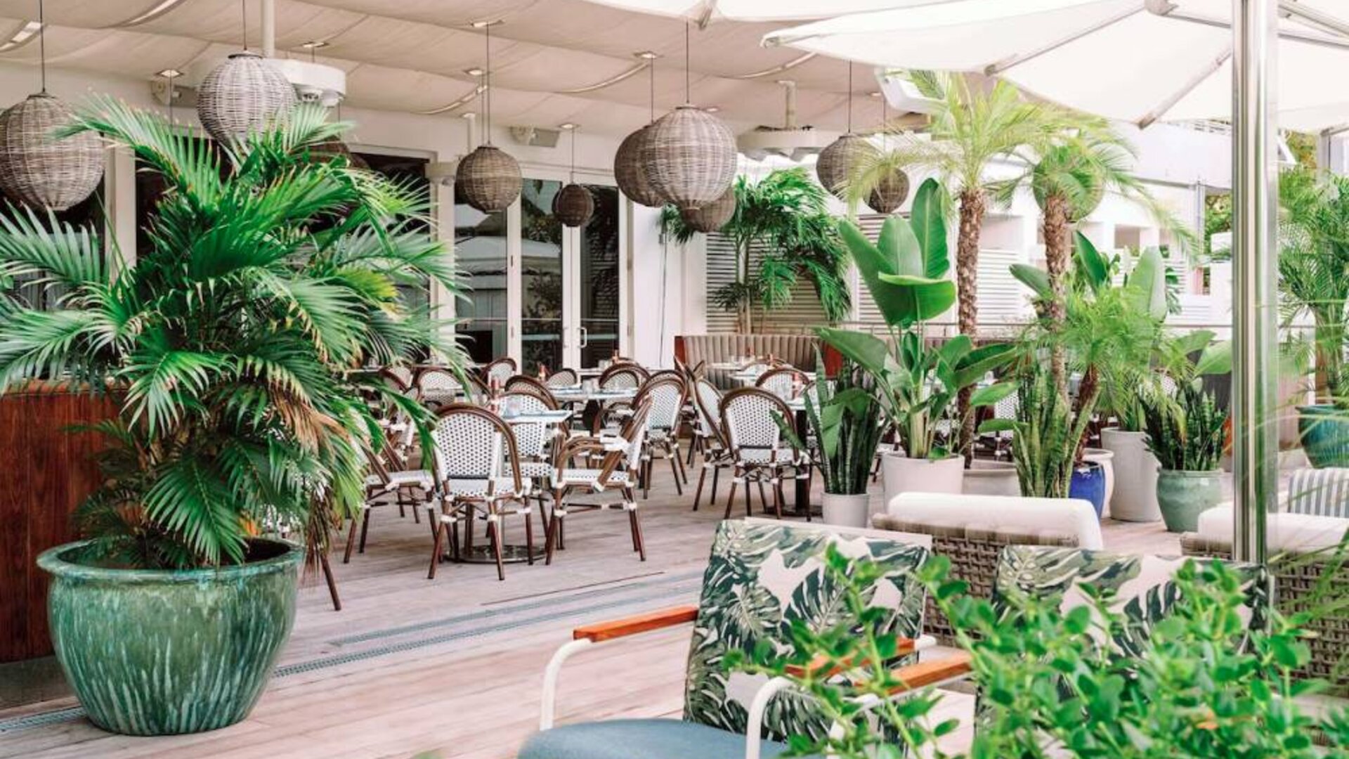 The hotel offers outdoor dining, with an abundance of plant life around the tables for four.