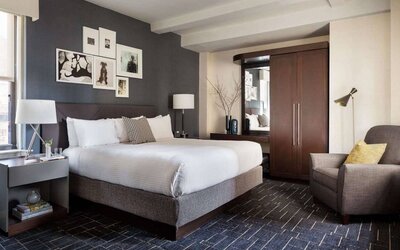 Double bed guest room in The Shelburne Sonesta New York, furnished with bedside lamp, wardrobe, and armchair.