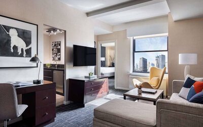 The Shelburne Sonesta New York guest room living area, including sofa, chairs, coffee table, and TV.