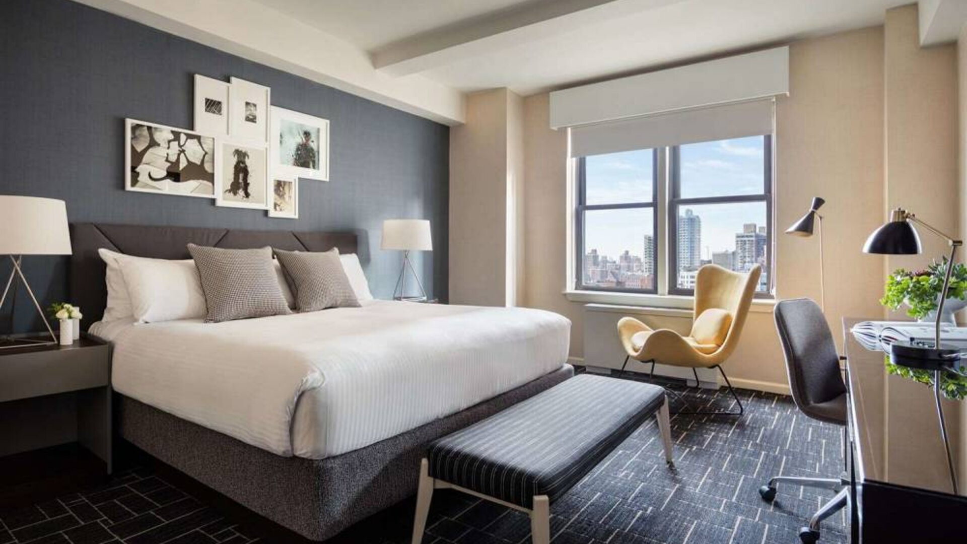 Double bed guest room in The Shelburne Sonesta New York, featuring a window, art on the wall, and a workspace desk, chair, and lamp.