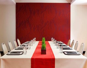 Meeting room in The Shelburne Sonesta New York, furnished with long table, 10 chairs around it, and a stark white and red color scheme.