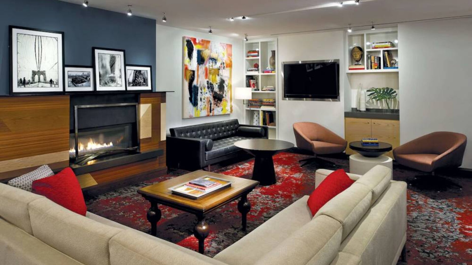 The Den’s lounge in The Fifty Sonesta Select New York features armchairs and sofas, coffee tables and a fireplace, plus a large TV.