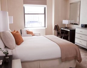 Double bed guest room in The Benjamin Royal Sonesta New York, furnished with TV, armchair, and workspace desk and chair.